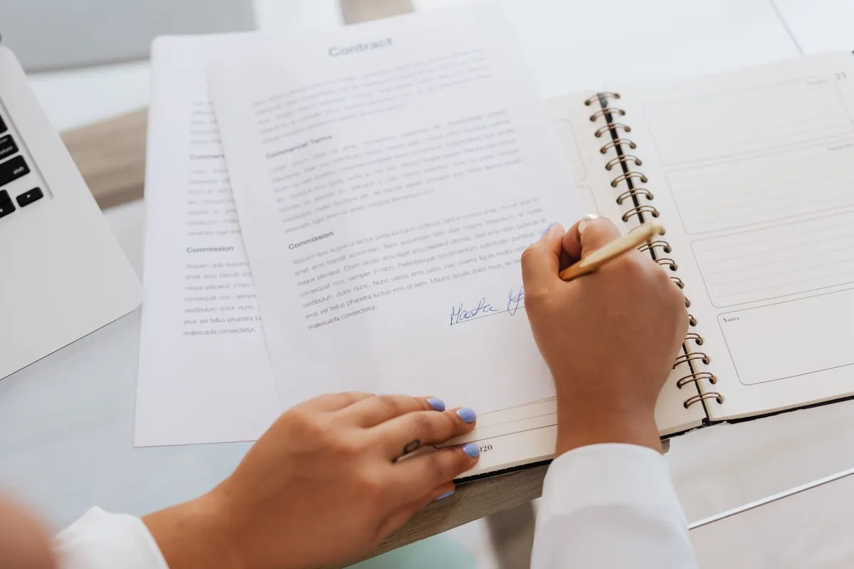 Close-up of hands signing a printed contract on a desk with office supplies
