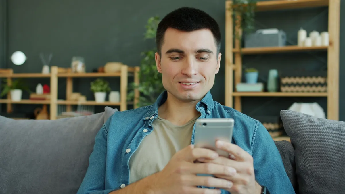 Man smiling while using a smartphone in a cozy living room
