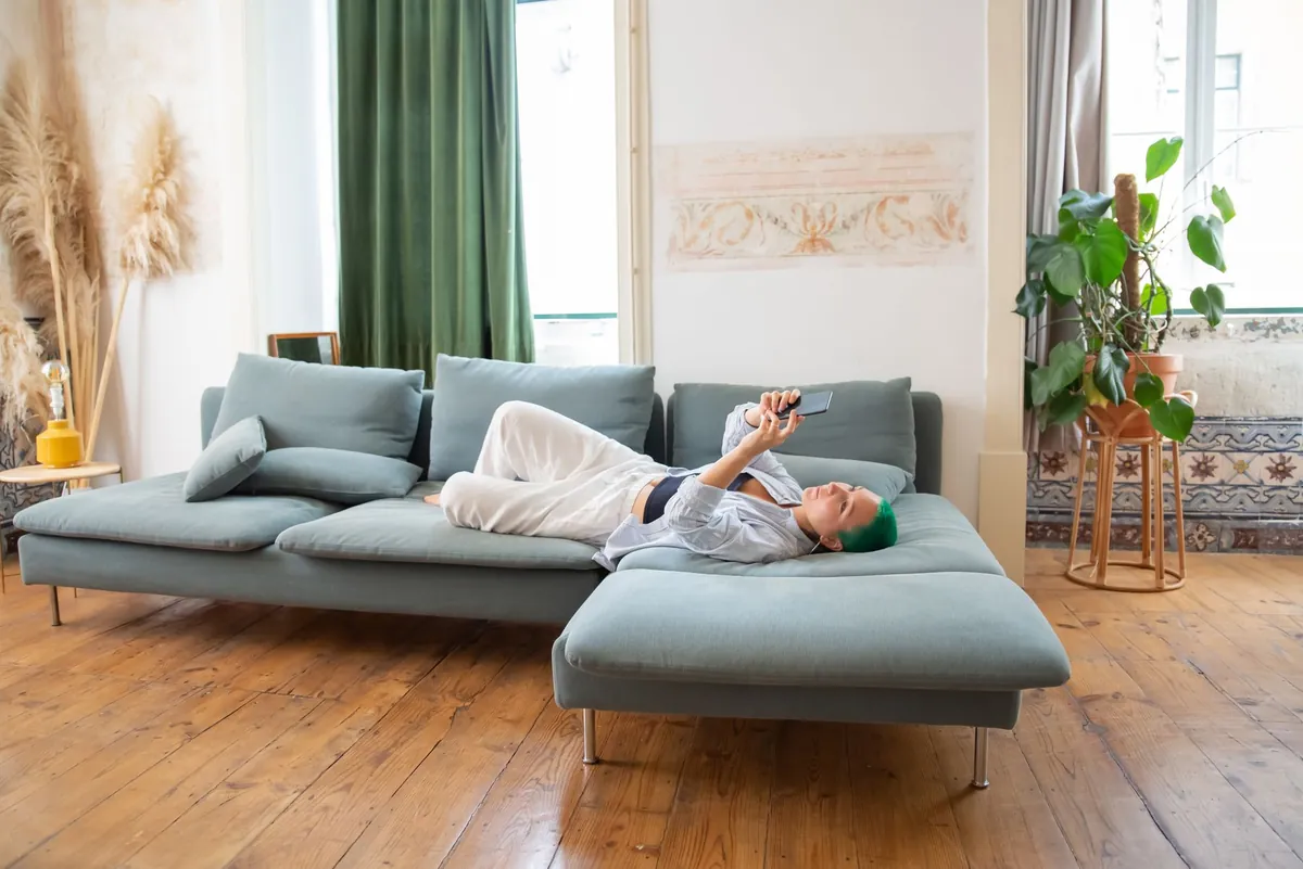 Woman with green hair lounging on a sofa at home using a smartphone