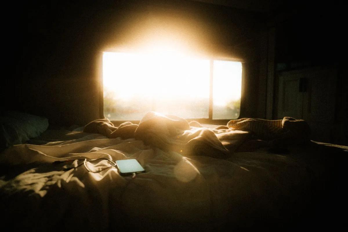 Smartphone lying on an unmade bed lit by bright morning sunlight from a window