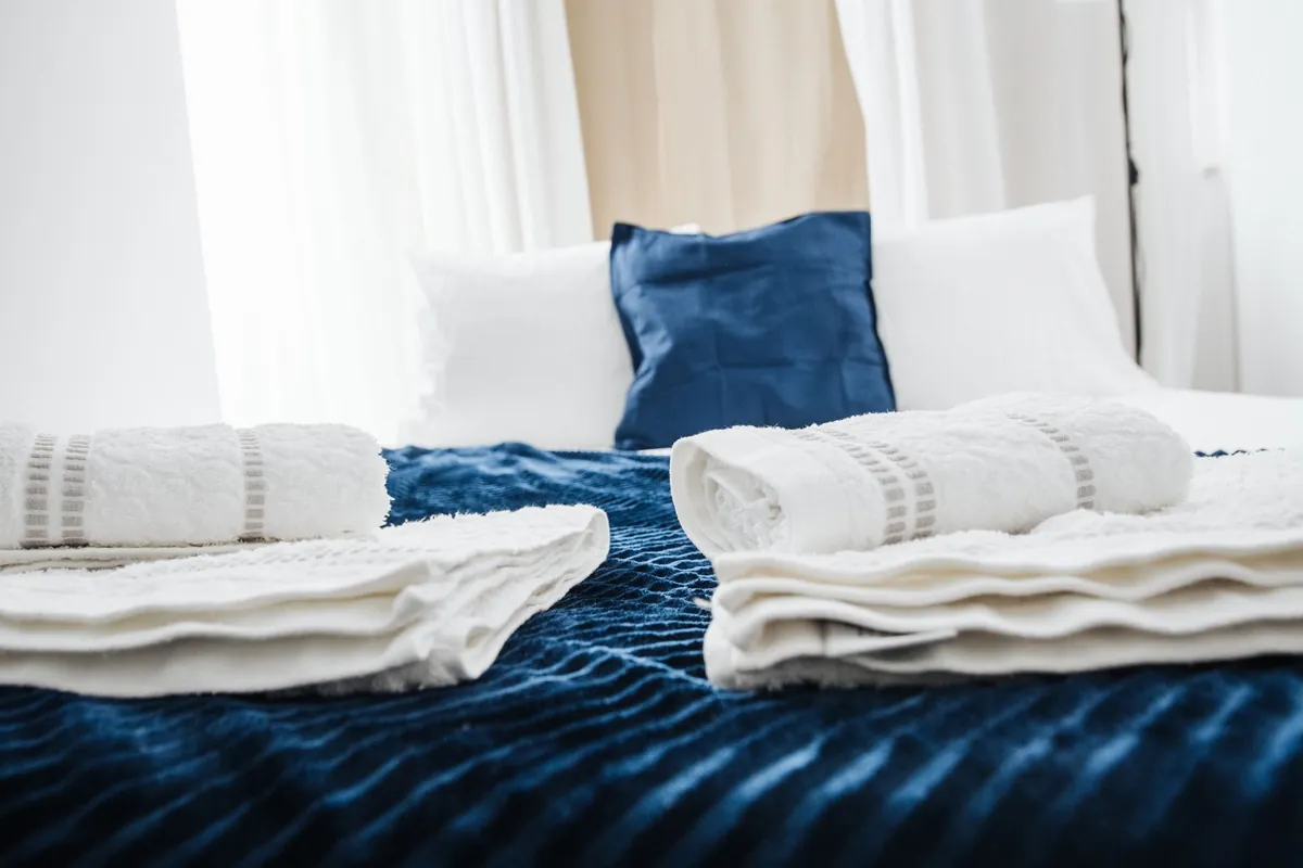 Folded white towels laid on a bed with a dark blue throw and pillows