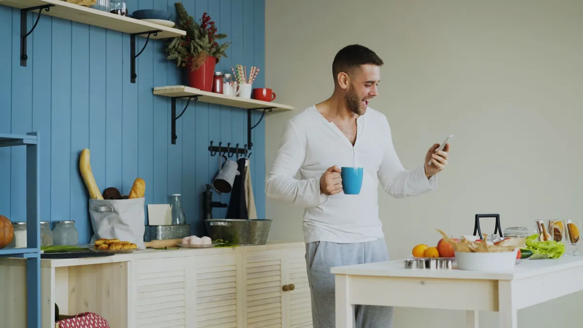Smiling man holds a mug and phone in a bright modern kitchen