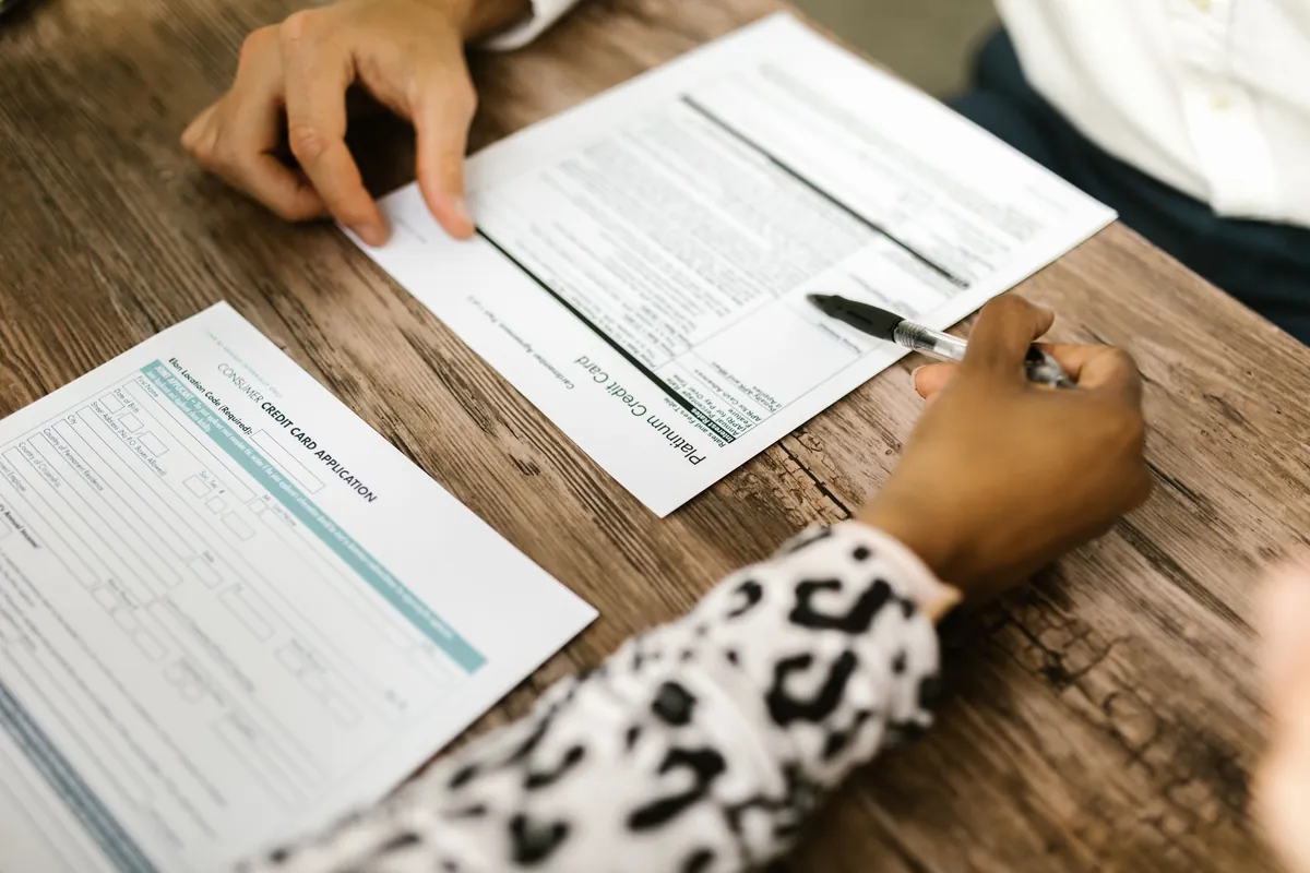 Two people reviewing and filling out a paper form on a wooden table