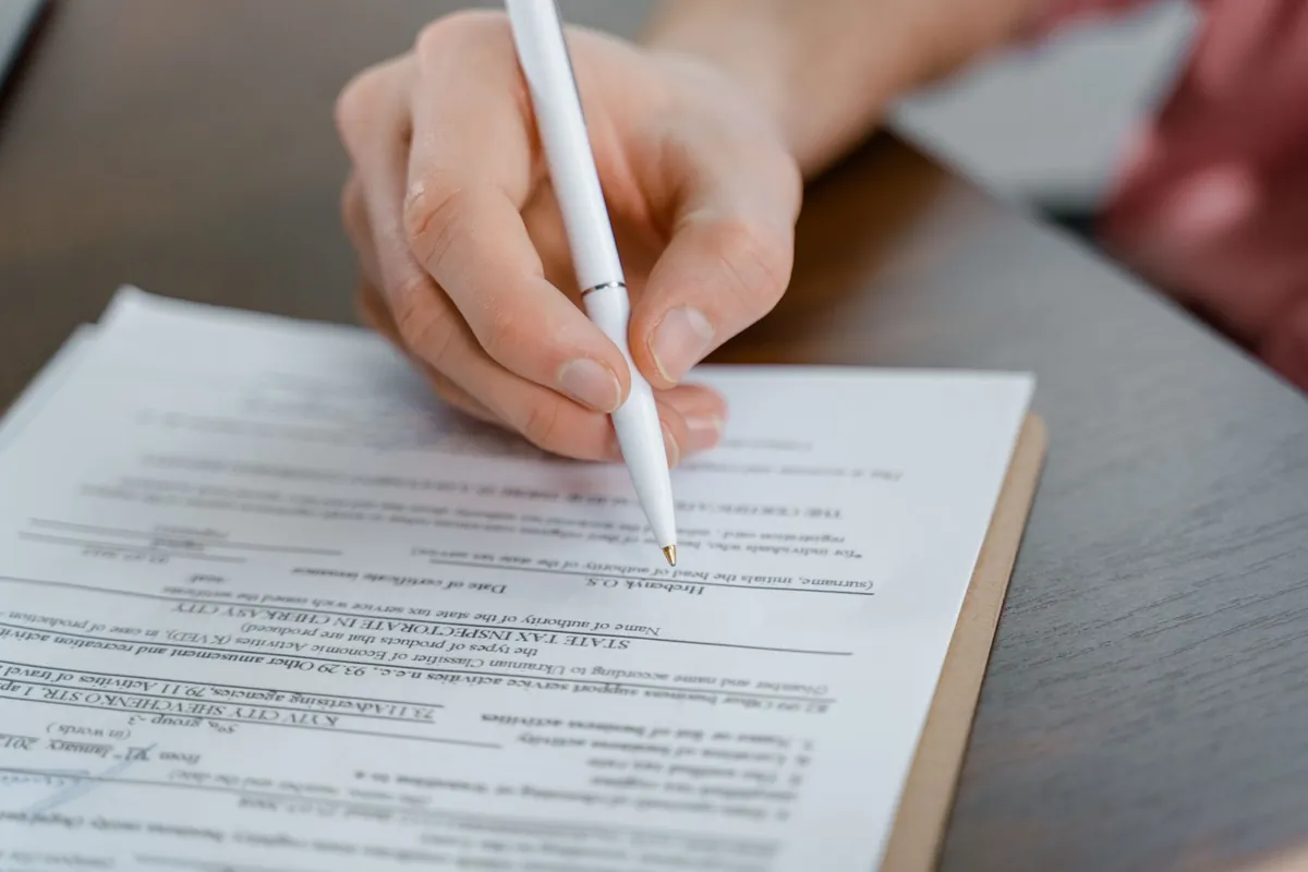 Close-up of a hand holding a pen signing a paper document