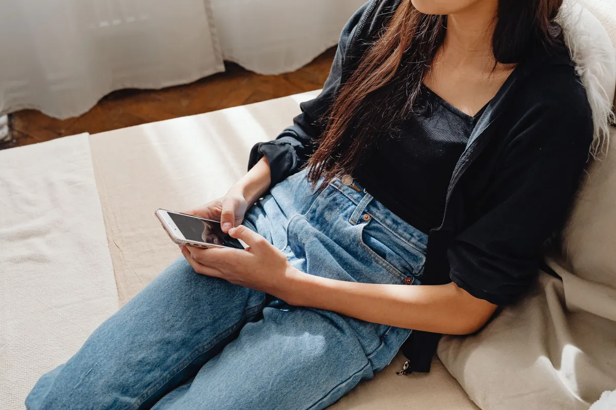 Young woman in casual clothes using a smartphone while sitting on a sofa indoors