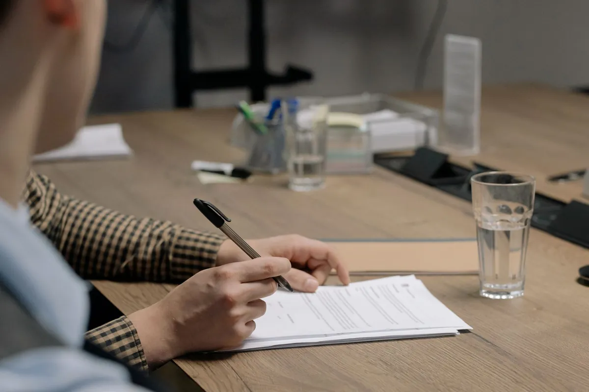Person in business attire signing a document at a wooden table in an office