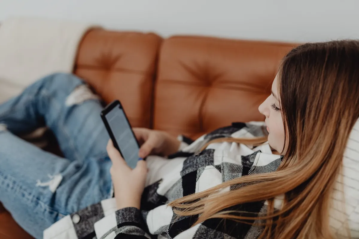 Woman lying on a leather sofa looking at her smartphone in a living room