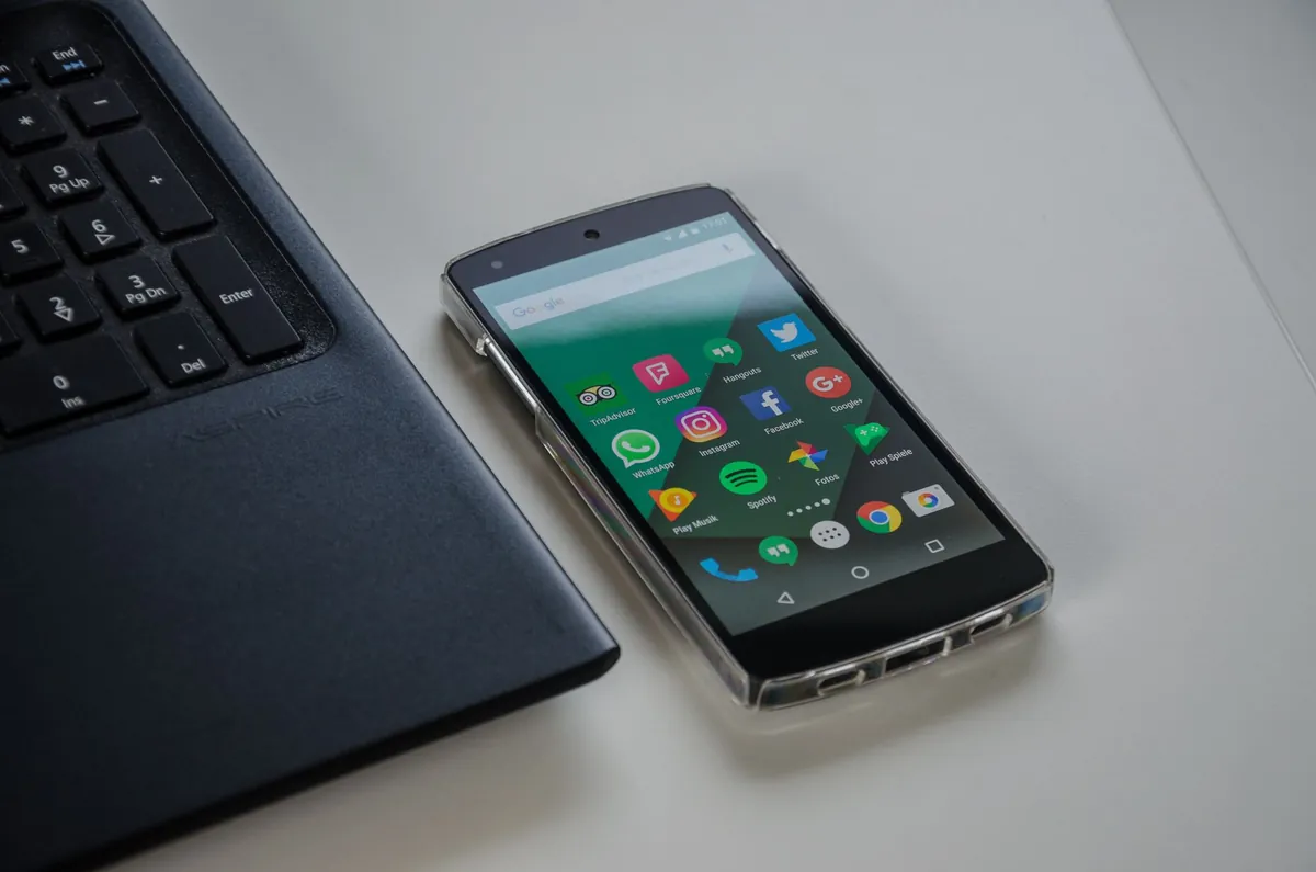Smartphone showing an app grid lying next to a laptop keyboard on a white desk