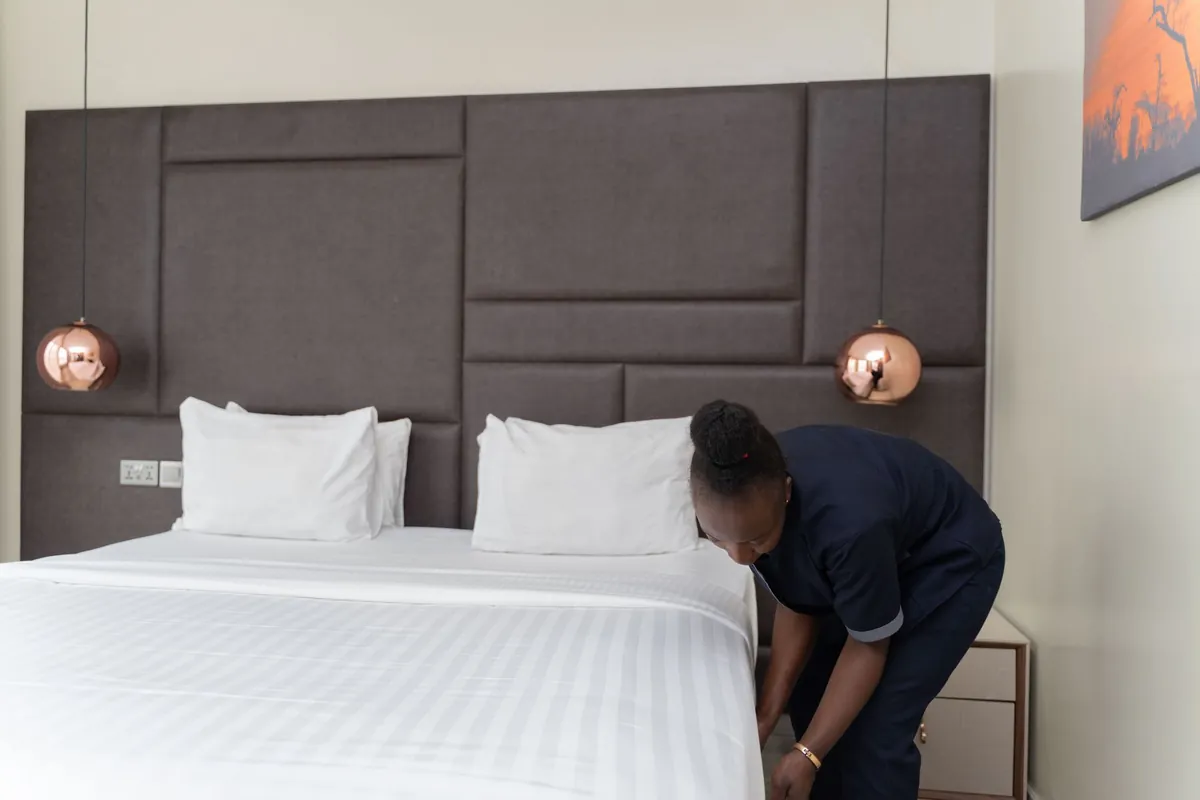 Hotel staff member smoothing white sheets on a bed in a modern hotel room
