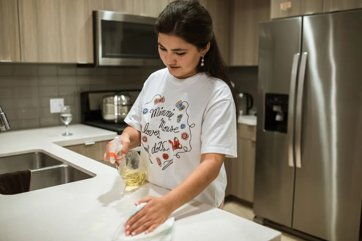 Young woman wiping down a kitchen counter with a cloth, indoors