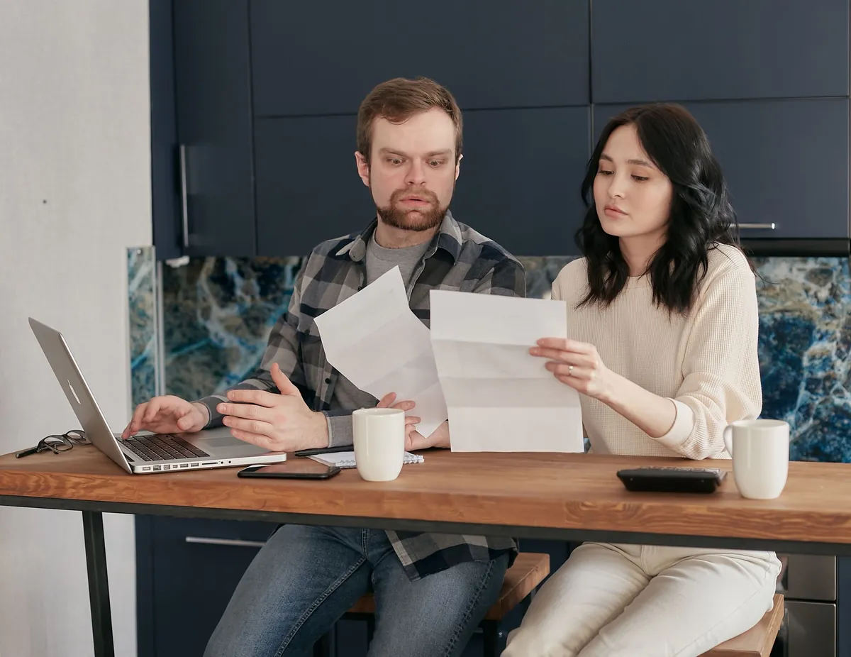 Couple at a wooden table reviewing documents with a laptop nearby