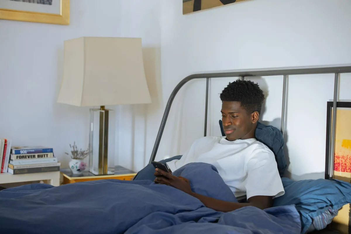 Young man in a white shirt using a smartphone in a cozy bedroom