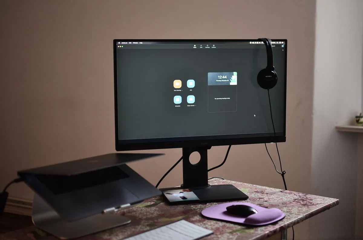 A laptop and smartphone resting on a wooden desk in a home office.
