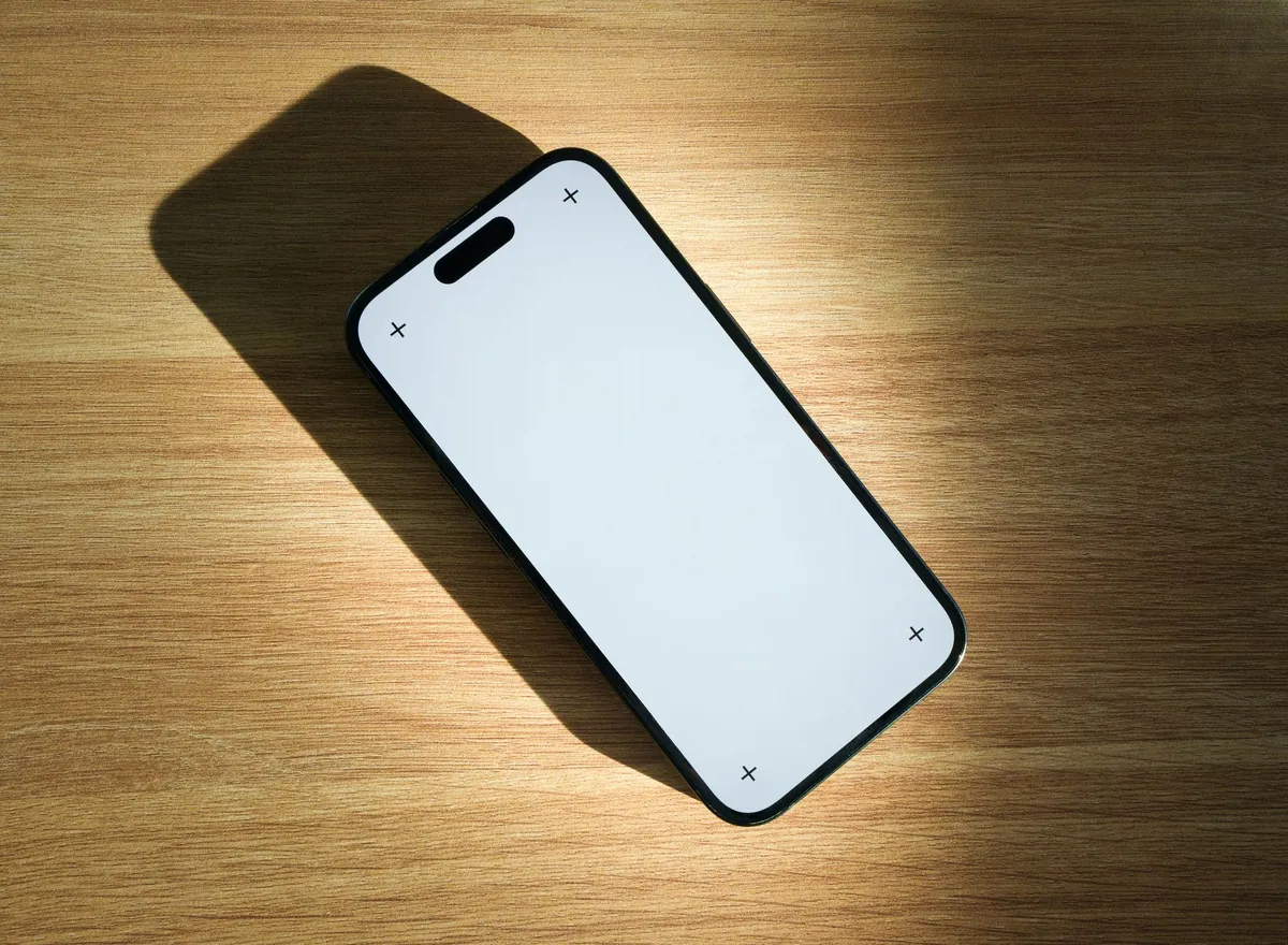 A smartphone with a blank white screen lying on a wooden table in warm light