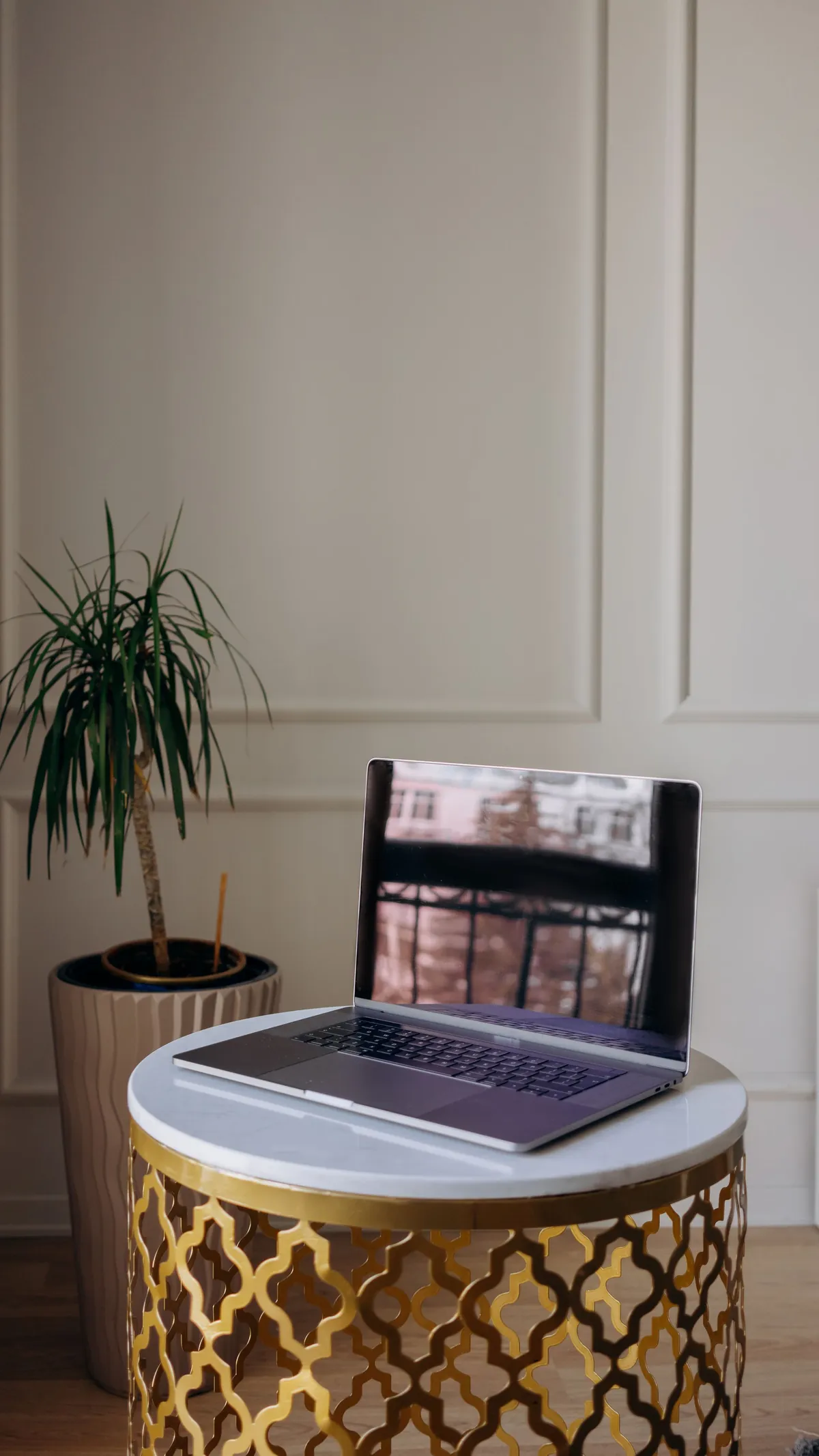 Open laptop on a small round table beside a potted plant