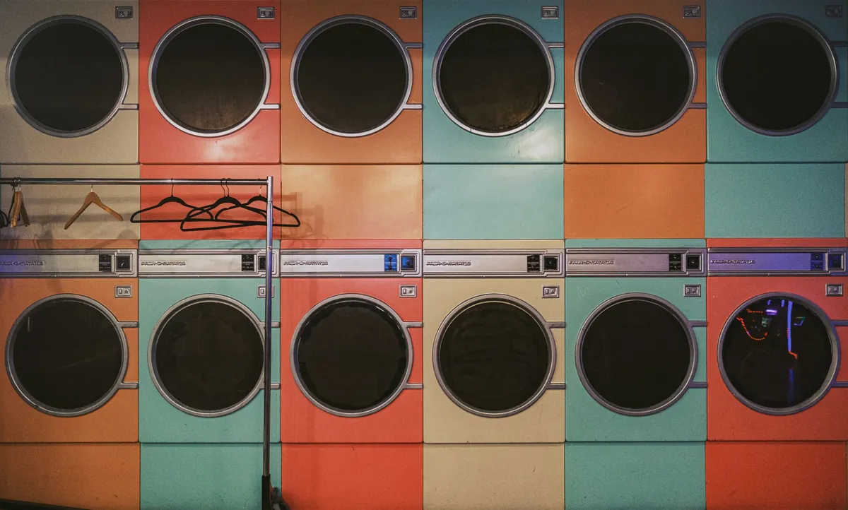Row of colorful vintage laundry machines with hangers inside a laundromat