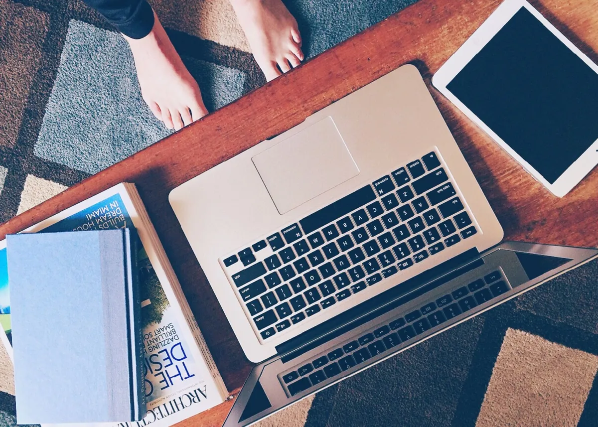 Overhead view of a laptop, tablet, books, and notebooks arranged on a wooden table