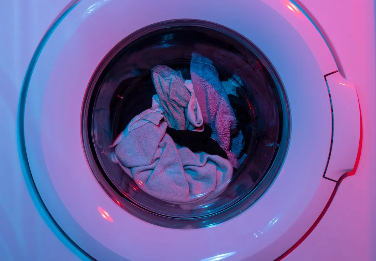 Clothes inside a front-loading washing machine lit with purple and blue light