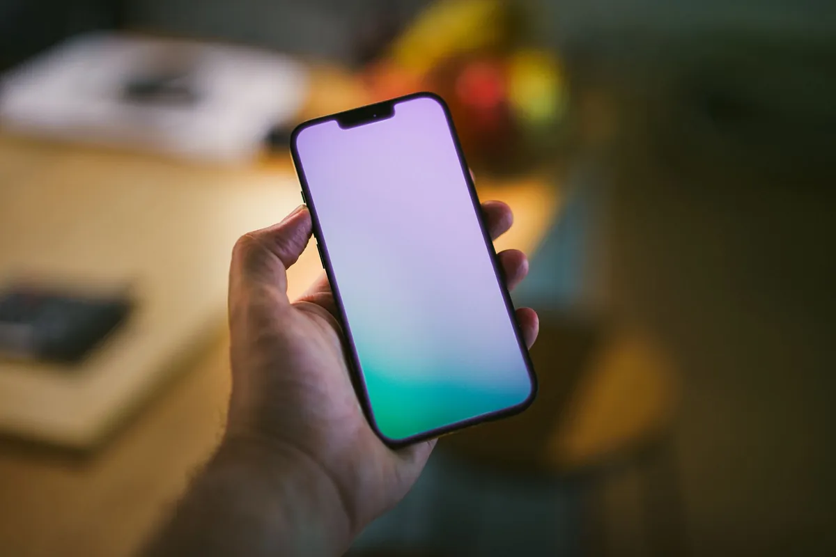 Hand holding a smartphone with a blank screen indoors