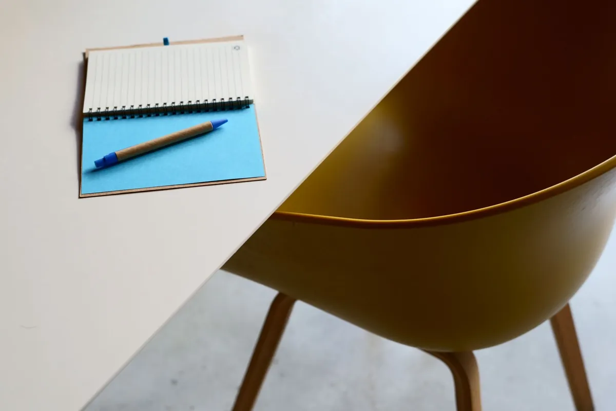 Minimalist workspace with an open notebook on a wooden table beside a yellow chair