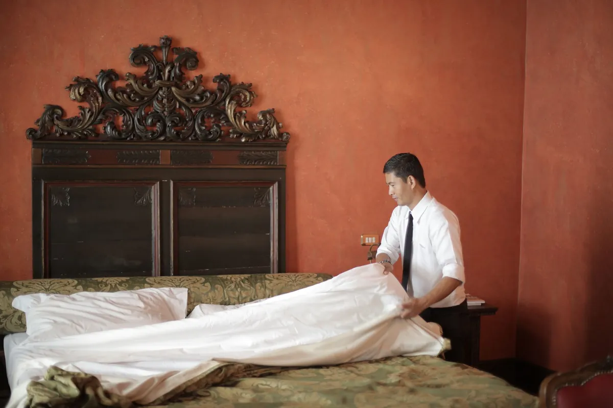 Man in a white shirt smoothing a white duvet on a bed in a room with red walls