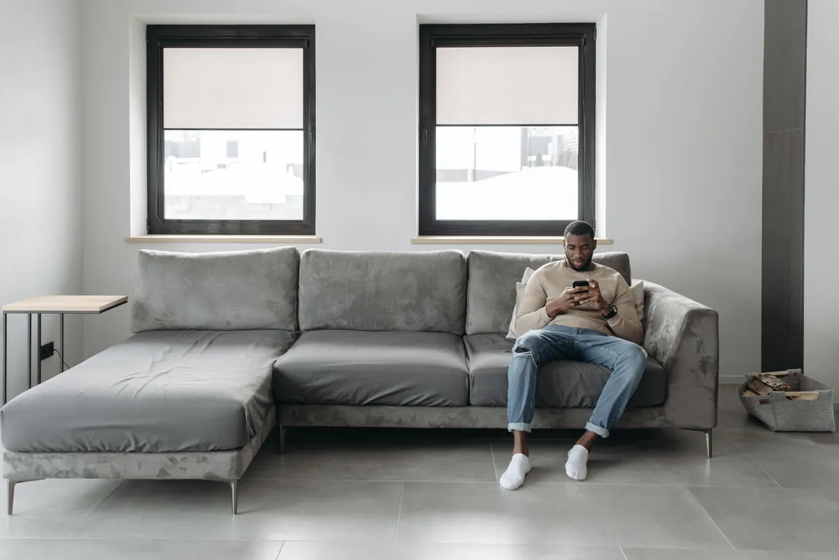 Man sitting on a sofa in a cozy living room, browsing on his smartphone