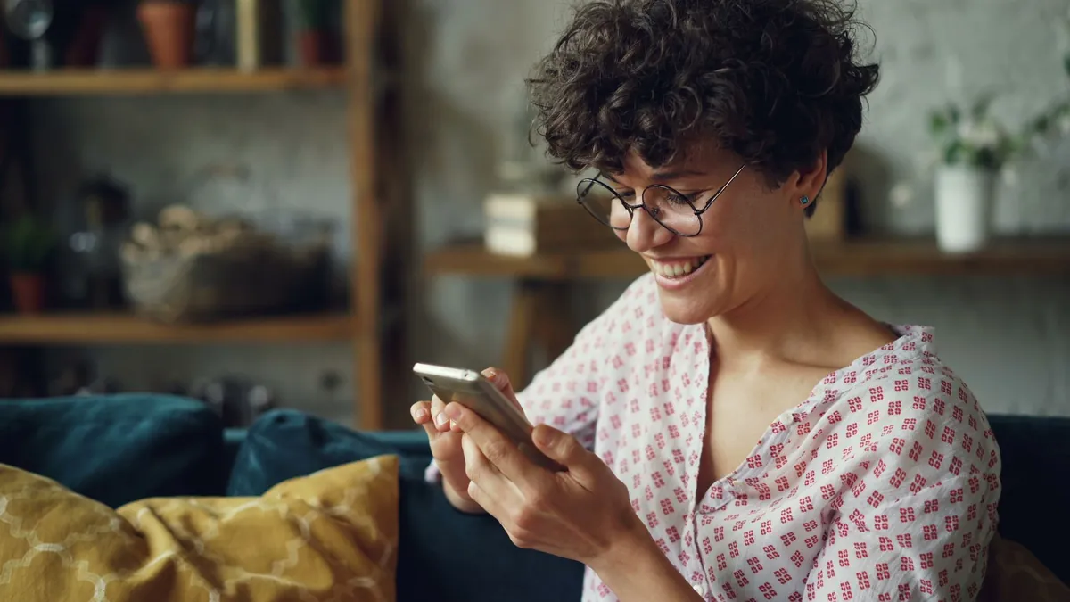 Smiling woman sitting on a sofa indoors while using her smartphone