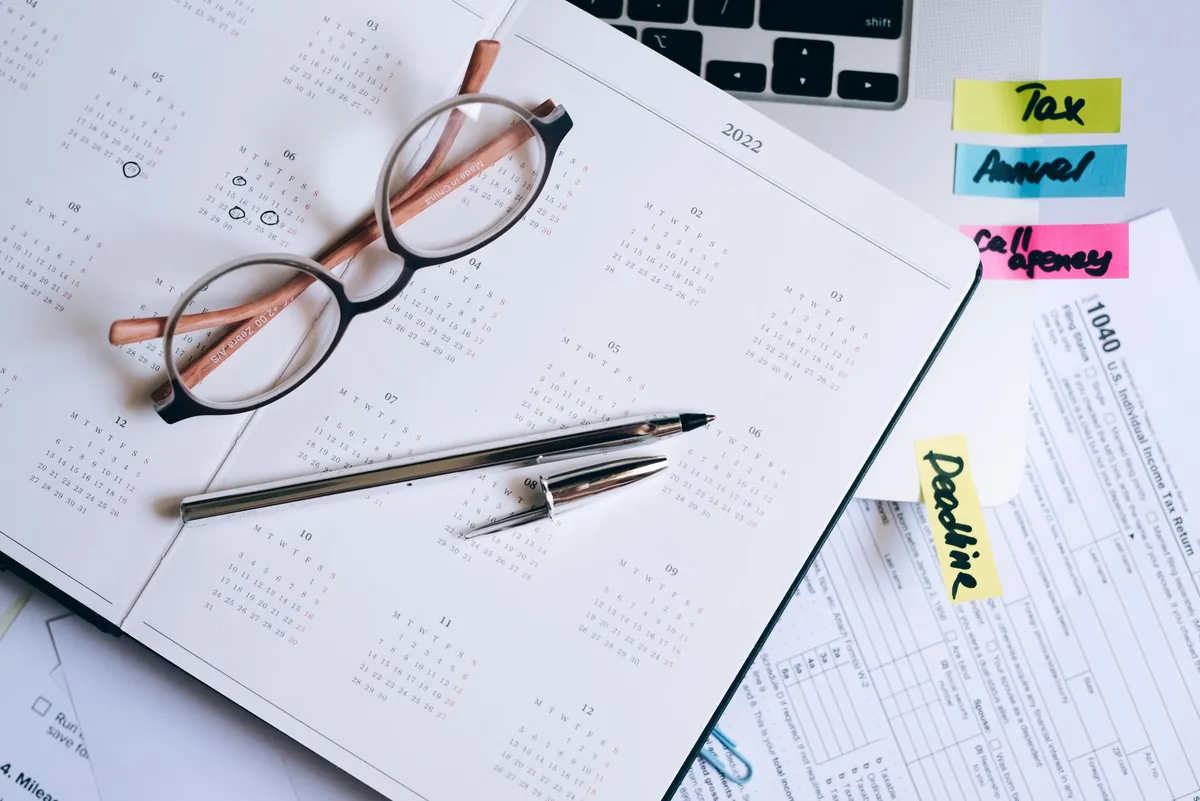 Eyeglasses, pens, a calendar, and tax documents arranged on a desk