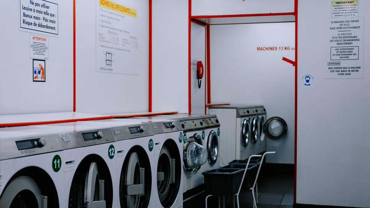 Row of front-loading washing machines beneath posted notices in a laundromat