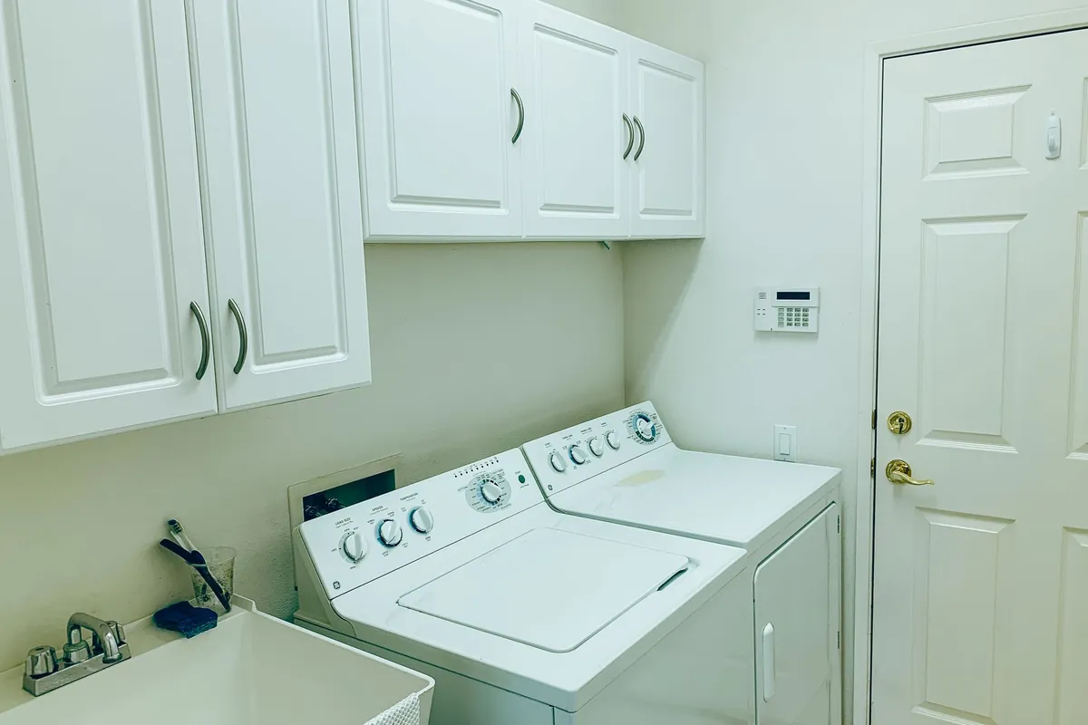 Organized laundry room with a washing machine, dryer, and white cabinets
