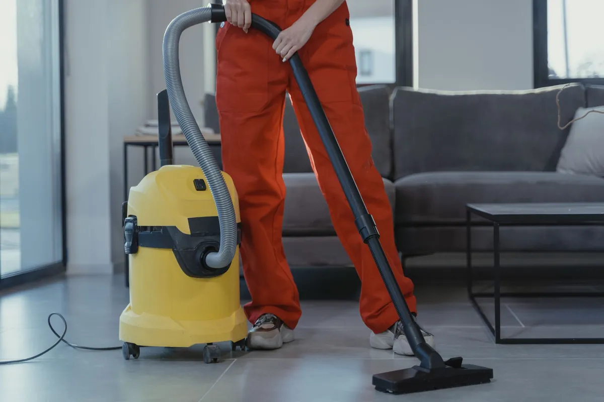 Cleaner vacuuming the carpet in a bright, tidy living room.