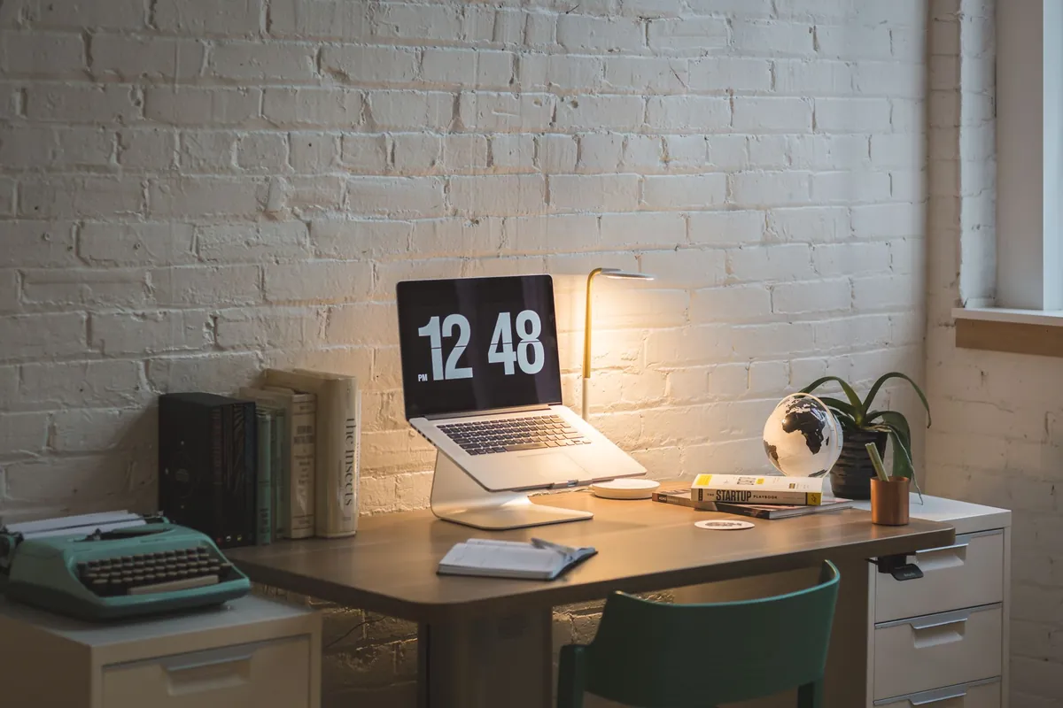 Laptop on a stand with notebook, books and typewriter on a wooden desk