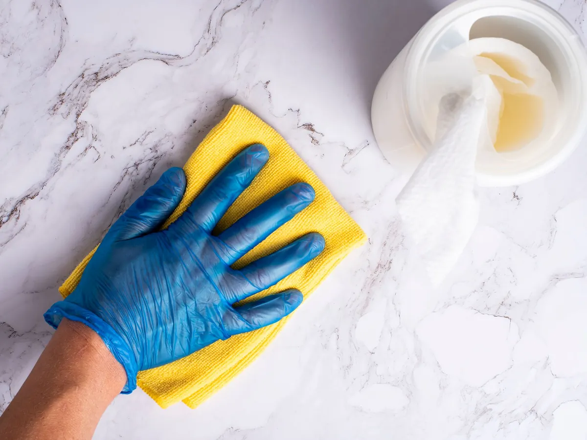 Gloved hand wiping a white marble-patterned surface with a yellow cloth