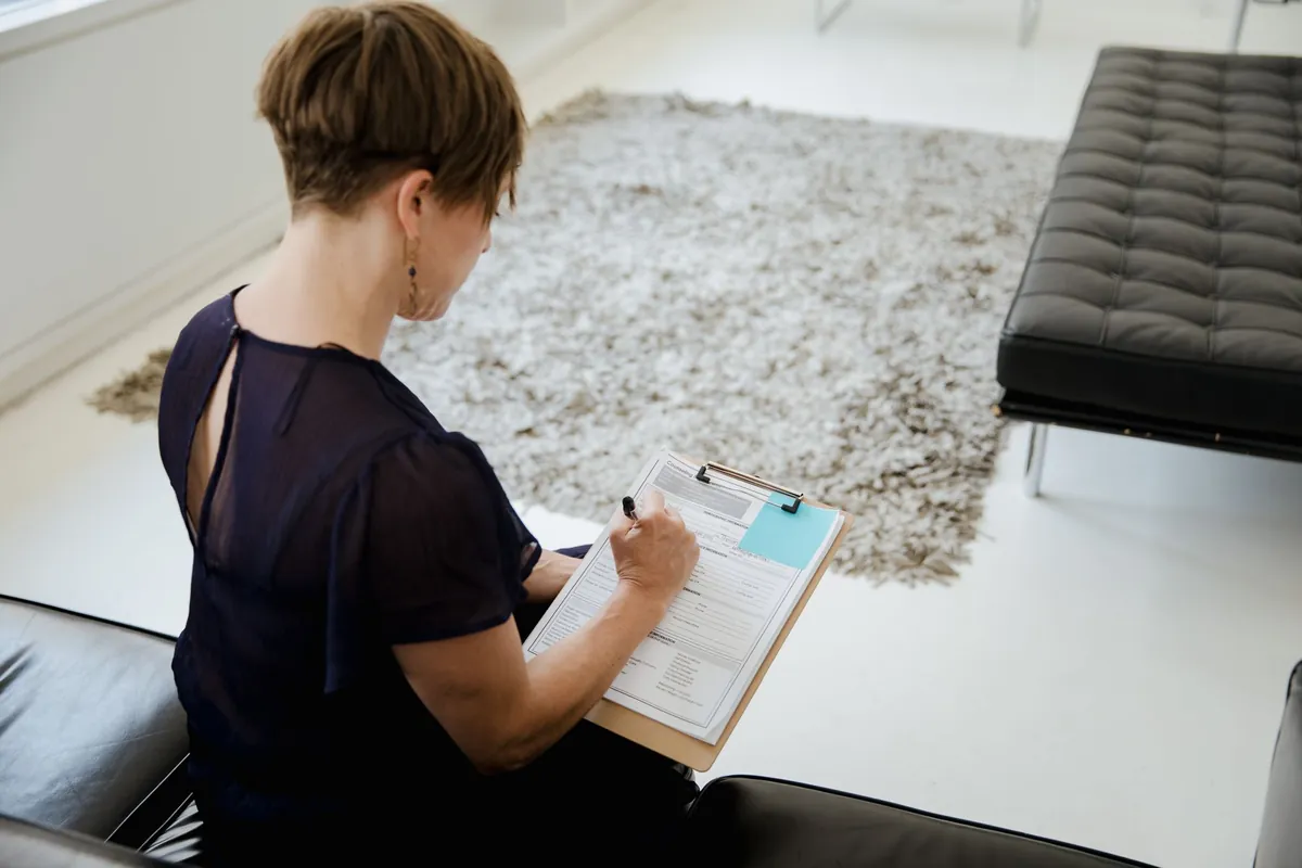 Woman sitting indoors writing on a clipboard at a table