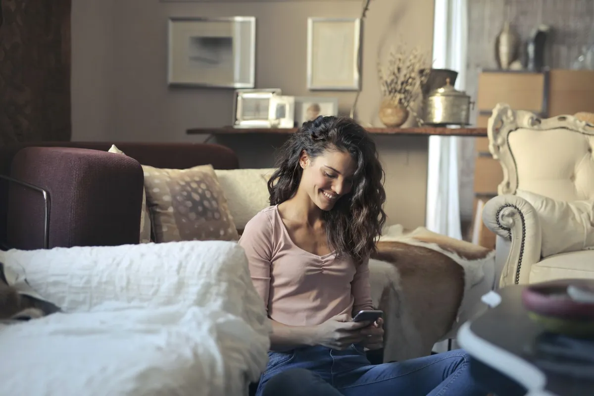 Smiling woman in casual clothes using her smartphone in a living room