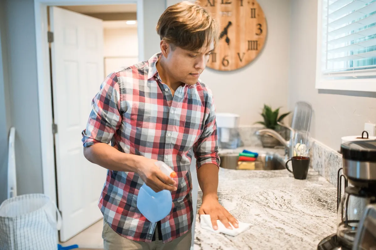 Man wiping a kitchen counter with a spray cleaner in a modern kitchen
