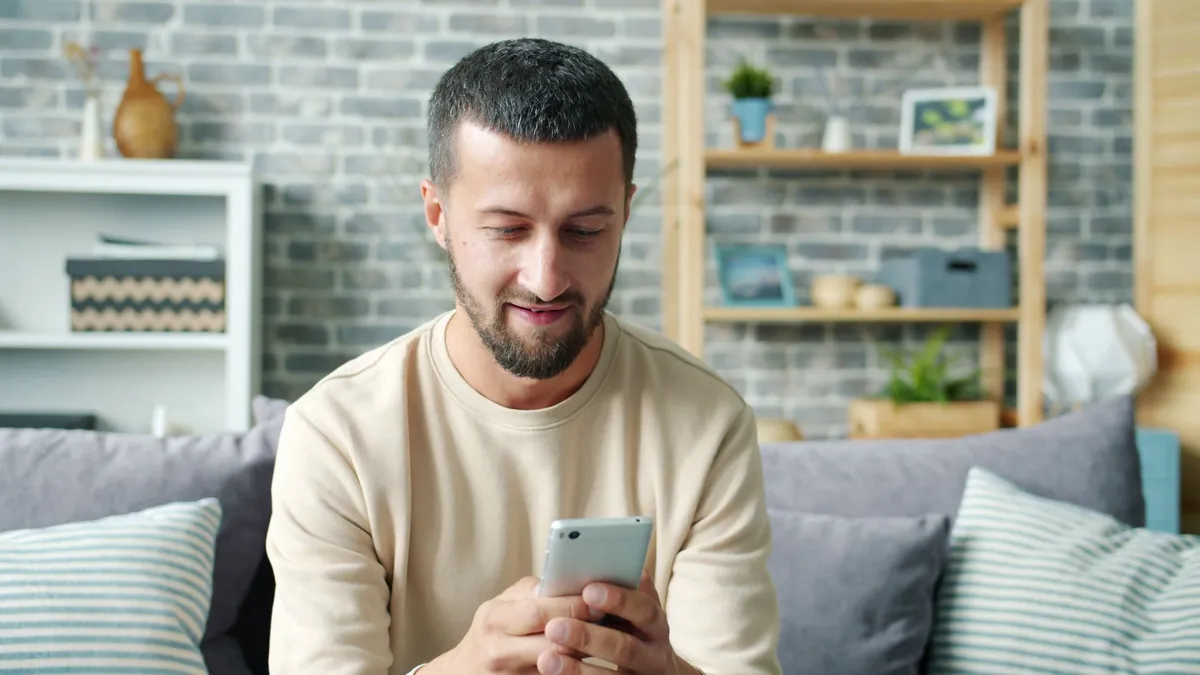 Man sitting on a sofa in a modern living room using his smartphone