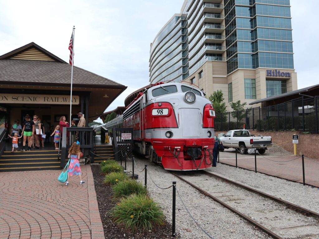 A vintage locomotive at a train station with tourists standing nearby in Branson, Missouri