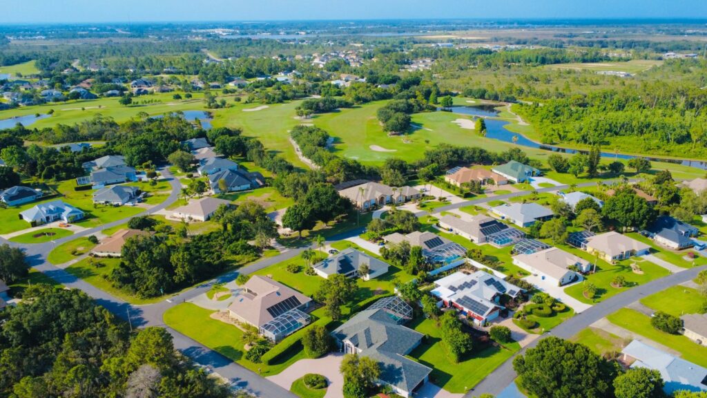 Aerial view of a sunny suburban neighborhood with green lawns and houses with solar panels