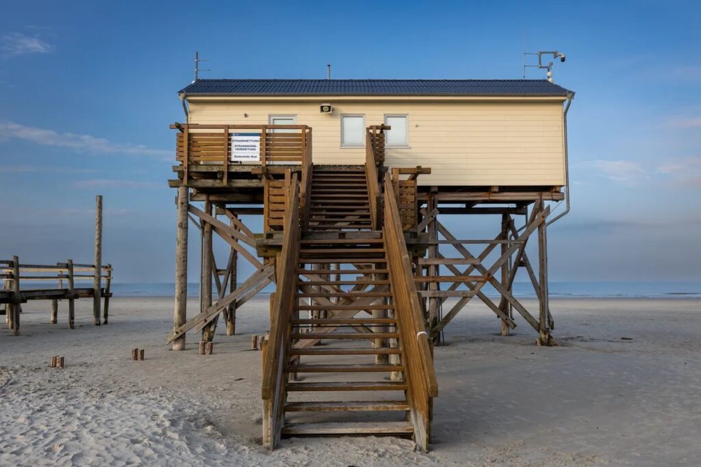 Beach house on tall wooden stilts with a long staircase leading down to sand under a blue sky