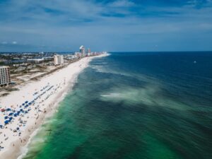 Aerial view of a white sand beach with umbrellas and beachfront condominium buildings along the water