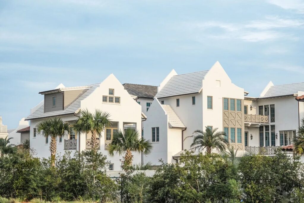 White coastal townhouses with steep gabled roofs and palm trees behind green dune plants