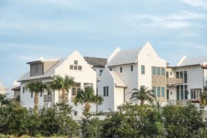 White coastal townhouses with steep gabled roofs and palm trees behind green dune plants