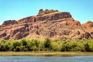 Red rock cliffs beside a river under a clear blue sky in a desert landscape