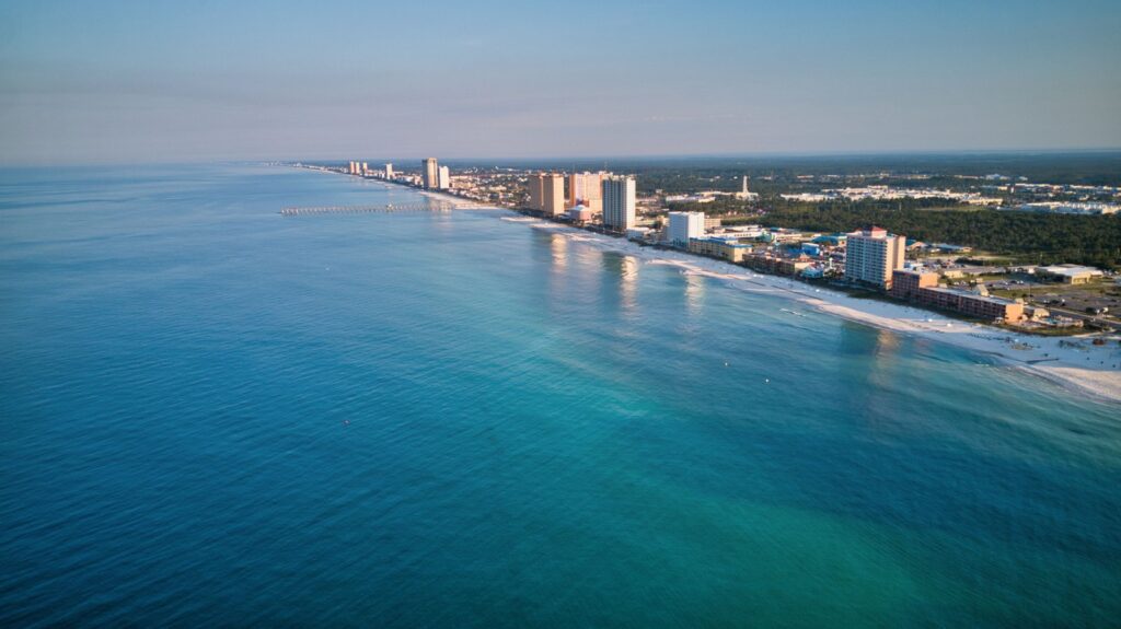 Aerial view of a beach coastline with clear blue water and tall buildings along the shore