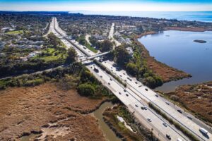 Aerial view of a coastal highway running beside a lagoon under a clear blue sky.