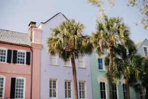 Row of pastel-colored historic homes with palm trees along a sunny Charleston street