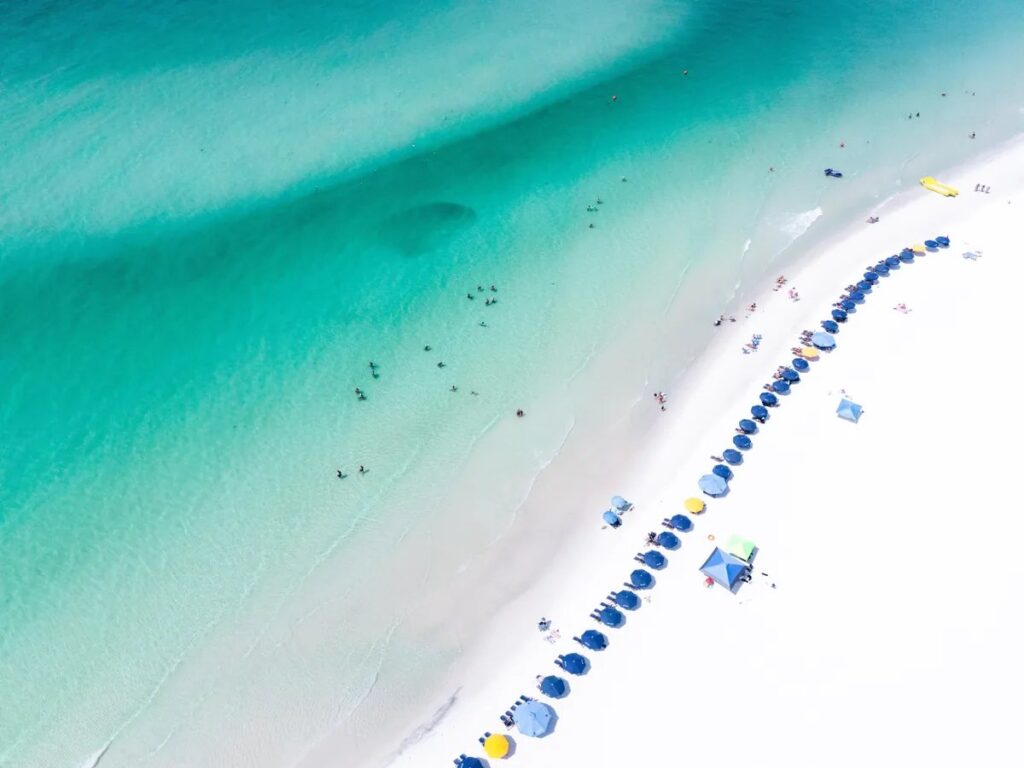 Aerial view of a white sand beach with emerald green water and rows of beach umbrellas