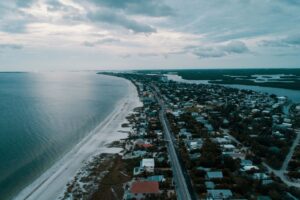 Aerial view of a coastal city with houses along a calm ocean under a cloudy sky.