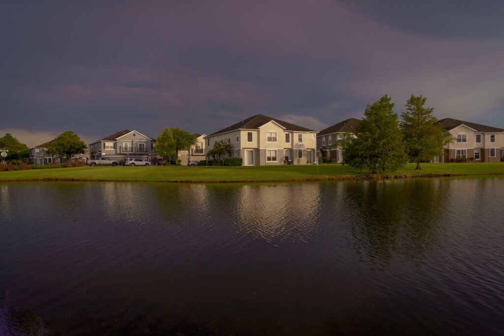 Lakefront homes reflecting on calm water under a dramatic cloudy sky